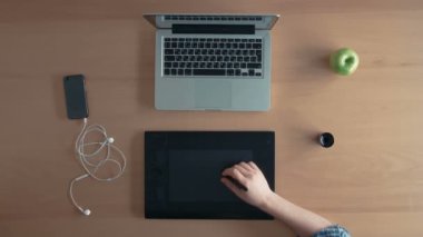 Üstten Görünüm Tasarımcısı adam veya Illustrator onun grafik tablet ve dijital tasarım oluşturma dizüstü kullanır ve bir elma yiyor