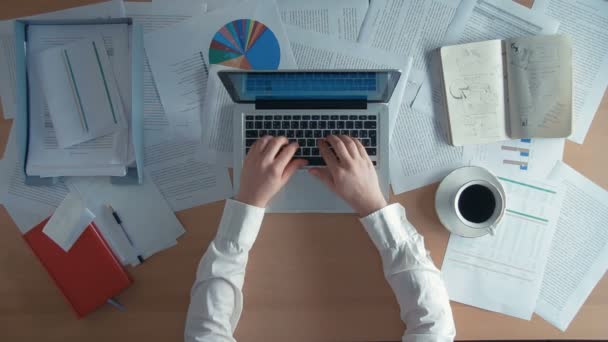 Top vista empresário trabalhando na mesa de escritório com seu laptop e beber café cercado por um monte de papelada e relatórios financeiros, cadernos — Vídeo de Stock