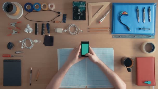 Bovenaanzicht softwareingenieur is met behulp van mobiele telefoon-smartphone op zijn bureau vol apparatuur groen scherm — Stockvideo