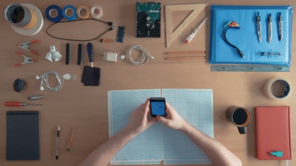 Engenheiro de software de visão superior está usando o smartphone do telefone celular em sua mesa cheia de equipamentos — Vídeo de Stock