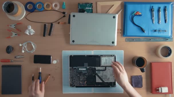 Технік-інженер зверху ремонтує ноутбук на своєму столі, оточений приладдям та обладнанням — стокове відео