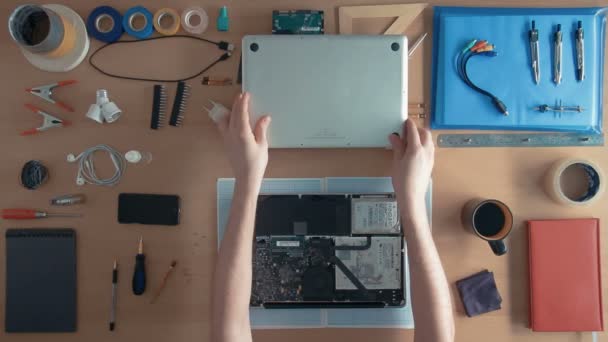 Ovanifrån tekniker reparerar bärbar dator på hans skrivbord omgiven av förnödenheter och utrustning — Stockvideo