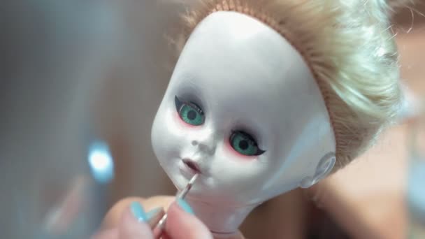Молодая женщина рисует куклу, делая ее страшной — стоковое видео