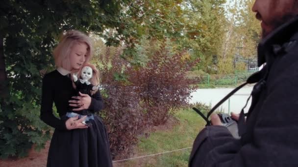 Tournage photo d'une jeune femme dans le caractère d'une fille effrayante au visage blanc avec une poupée — Video