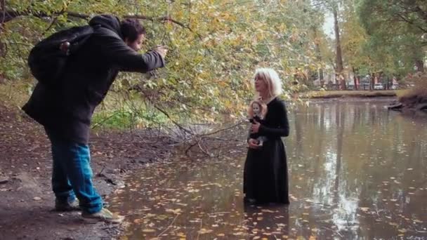 Sesión de fotografía de una joven en el personaje de una niña de cara blanca aterradora con una muñeca dentro de un estanque — Vídeo de stock