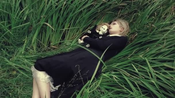 Стилізований постріл моторошна біла обличчям жінки з лялькою в траві в лісі лежачи — стокове відео