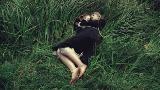 Стилізований постріл моторошна біла обличчям жінки з лялькою в траві в лісі лежачи — стокове відео