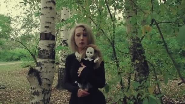 Plan stylisé femme au visage blanc effrayant avec une poupée dans l'herbe dans les bois — Video