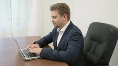 Dizüstü bilgisayar önünde ofisinde çalışan genç işadamı