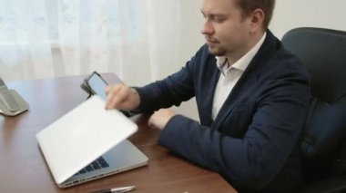 Dizüstü bilgisayar önünde ofisinde çalışan genç işadamı sonra onun dijital dokunmatik tablet alır ve kullanmaya başlar.