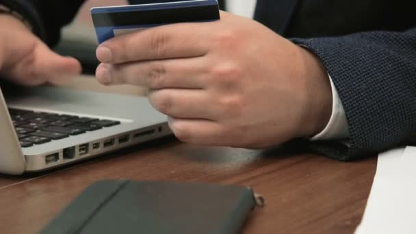 Jonge zakenman doet online winkelen in zijn kantoor houden een credit card en een getal te typen in de web-site — Stockvideo