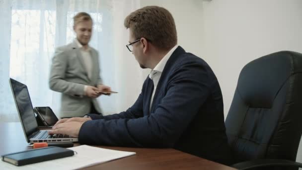 Junge Geschäftsleute im Büro tippen auf der Tastatur an seinem Laptop-Computer und seine Kollegen arbeitet kommt und bittet, die Dokumente zu unterzeichnen — Stockvideo