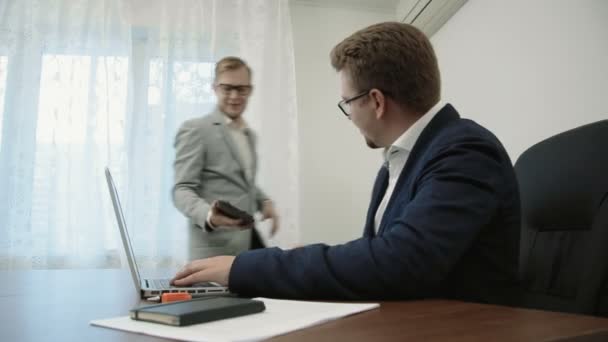 Jungunternehmer, die im Büro vor dem Laptop sitzen, kommen in den Raum und zeigen ihm Informationen auf einem digitalen Touchscreen-Tablet-Computer, auf dem sie arbeiten. — Stockvideo