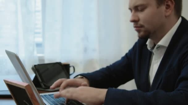 Jovem empresário trabalhando em seu escritório em frente ao computador portátil. Em seguida, olha para a foto de sua família leva, sorri e continua trabalhando — Vídeo de Stock