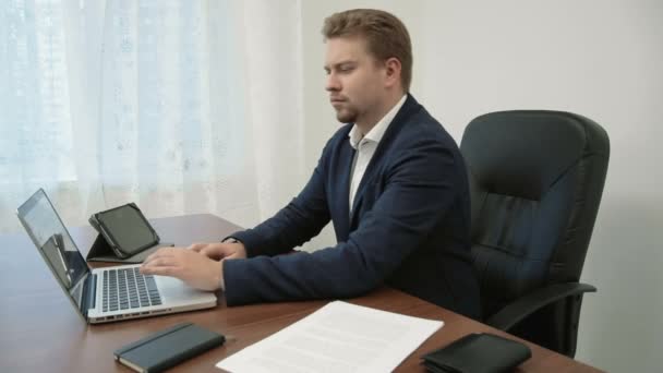 Junger Geschäftsmann beim Online-Einkauf in seinem Büro vor dem Laptop nimmt seine Brieftasche und zählt die Rechnungen, nickt dann zufrieden — Stockvideo