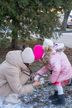 Çocuklar, aileleriyle karda neşeyle oynuyorlar. Küçük kar figürleri yapıyorlar. Sahne arka planda ağaçlar olan bir kış harikalar diyarında geçiyor..
