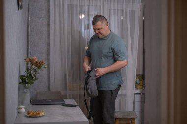 Bir adam akşamleyin evinden ayrılmaya hazırlanıyor. O, bir vazo ve dizüstü bilgisayarla birlikte bir masada. Odaklanmış ve sakin görünürken çantasını topluyor..