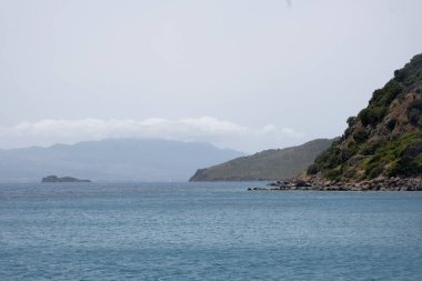 İnsanlar deniz kıyısındaki bir tatil köyünde eğleniyorlar. Manzara, gökyüzünde bulutlar olan tepeleri ve suyu kapsıyor. Rahatlatıcı atmosfer burayı boş zaman geçirmek için uygun bir yer haline getiriyor..