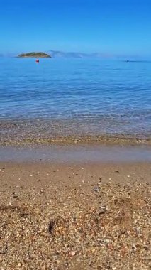 Deniz kenarında güneşli bir günde, yumuşak dalgalar ve güzel doğa ile kumsalda rahatlatıcı anların tadını çıkarın.