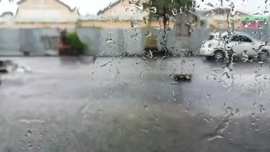 Şiddetli yağmurda açık hava manzarası, su damlacıklarıyla ıslanmış bir pencereden görülüyor.