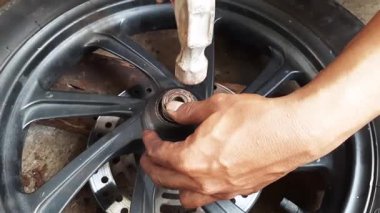 Tamirci, otomotiv bakım ve ulaşım aracını tamir etmek için mekanik beceriler sergileyen bir tamircide motosiklet tekerindeki konumu kaldırmak için çekiç kullanıyor..