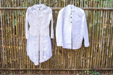 Gelinlik ve damat kıyafeti bambu bir çitte sergileniyor. Geleneksel giysiler, bağlılığı ve yeni bir bölümün başlangıcını sembolize ediyor..