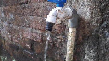 Musluk, değerli bir kaynağın atığını ve tesisat tamir ihtiyacını gösteren dokulu tuğla bir duvara doğru yavaşça damlıyor..