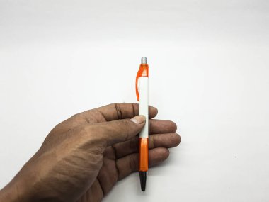 Koyu tenli bir el, beyaz ve turuncu plastik bir tükenmez kalemi, parlak beyaz bir arkaplana karşı sıkıca kavrıyor. Bu da belgeleri yazmaya ya da imzalamaya hazır olduğunu gösteriyor..