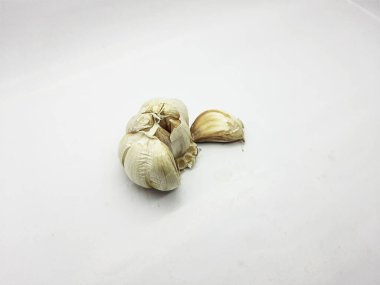 Garlic bulb and one separate clove rest diagonally on a bright white surface emphasizing simple food ingredient photography against ample copy space.