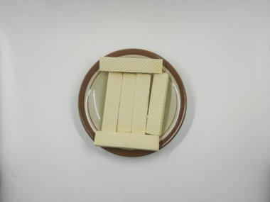 Yığılmış vanilyalı gofret kurabiyeleri küçük yuvarlak bir seramik tabakta dinleniyor. Kahverengi süslemeli, parlak beyaz arka planda..