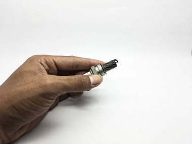 Tamirci el, motor tamirini temsil eden parlak beyaz bir arka plana karşı eski ve kirli bir buji parçası tutuyor..