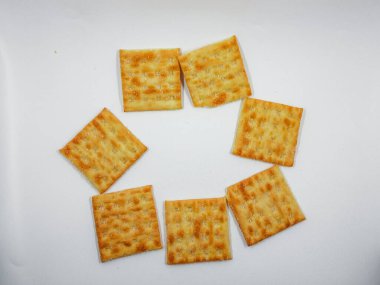 Tuz kristalli altın kare krakerler, basit ve çekici bir abur cubur gösterisi için el değmemiş beyaz bir zemin üzerinde dairesel bir desen şeklinde düzenlenmiştir..