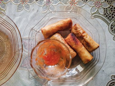 Kızarmış börekler şeffaf bir cam tabakta küçük bir kase canlı portakallı tatlı biber sosunun yanında düzenlenir..