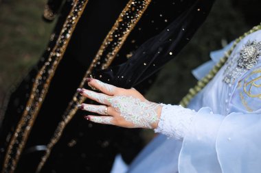 Karmaşık beyaz kınalı gelin eli zarif bir alyans içerir. Güzelliği, geleneği ve kutsal evlilik bağını sembolize eder..