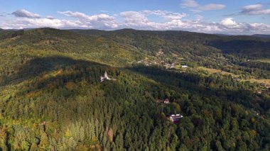 A breathtaking aerial perspective showcases a vibrant and lush green forested valley, flanked by hills and clouds above