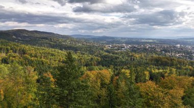 The breathtaking view showcases vibrant green forests along with a picturesque town beneath a dramatic, cloudy sky