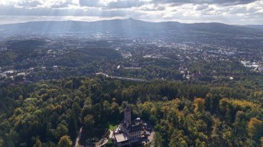 Aerial view showcases a vibrant forest beside a sprawling city under clouds, blending nature and urban beauty