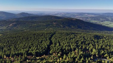 A stunning aerial view showcasing a vibrant forest landscape with rolling hills and beautiful blue skies