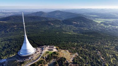 Nefes kesen bir hava manzarası, açık mavi gökyüzünün altında yemyeşil tepelerin arasında duran etkileyici bir kuleyi gözler önüne seriyor.