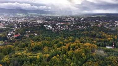 This aerial view showcases a vibrant cityscape surrounded by green forests beneath a picturesque sky
