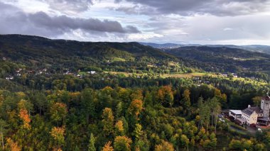 A breathtaking aerial landscape showcasing beautiful green hills, vibrant autumn foliage, and an ancient structure
