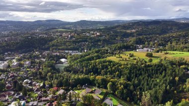 This stunning aerial view shows lush green hills intertwined with vibrant urban areas under a cloudy sky