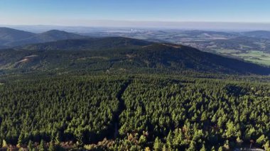 A stunning aerial view showcasing a vibrant forest landscape with rolling hills and beautiful blue skies