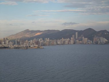 Uzak gökdelenleri olan sakin bir sahil manzarası, uzak yüksek binalarla okyanus üzerinde sakin bir ufuk.