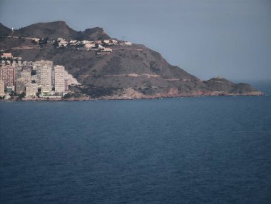 Sahil manzarası, huzur dolu körfeze bakan güzel kayalık binalar ve yelkenli gemiler.