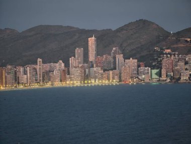 Akşam deniz kenarındaki ışıklar pırıl pırıl, alacakaranlık siluetleri parlak kıyı şeritleri ve huzur dolu