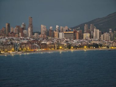 Aydınlatılmış kuleleri, parıldayan deniz feneri yansımalarıyla sakin kıyı manzarası olan parlak deniz kenarı.