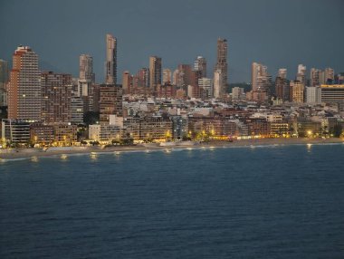 Şehir kıyı şeridinde gün batımı parıldıyor, akşam şehir silüeti yansıtıcı okyanus yüzeyi atmosferiyle birlikte.