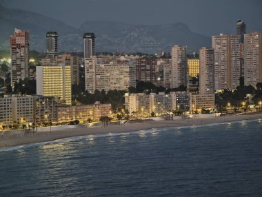Aydınlatılmış otellerle sakin deniz manzarası, parlayan ışıklarla ve uzak mesafelerle sakin sahil manzarası