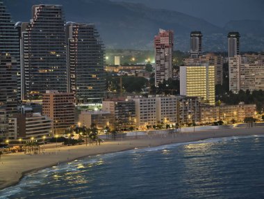 Liman ufku gün batımında ışıldıyor, günbatımı sakin sahil üzerinde parlayan liman silüetiyle.